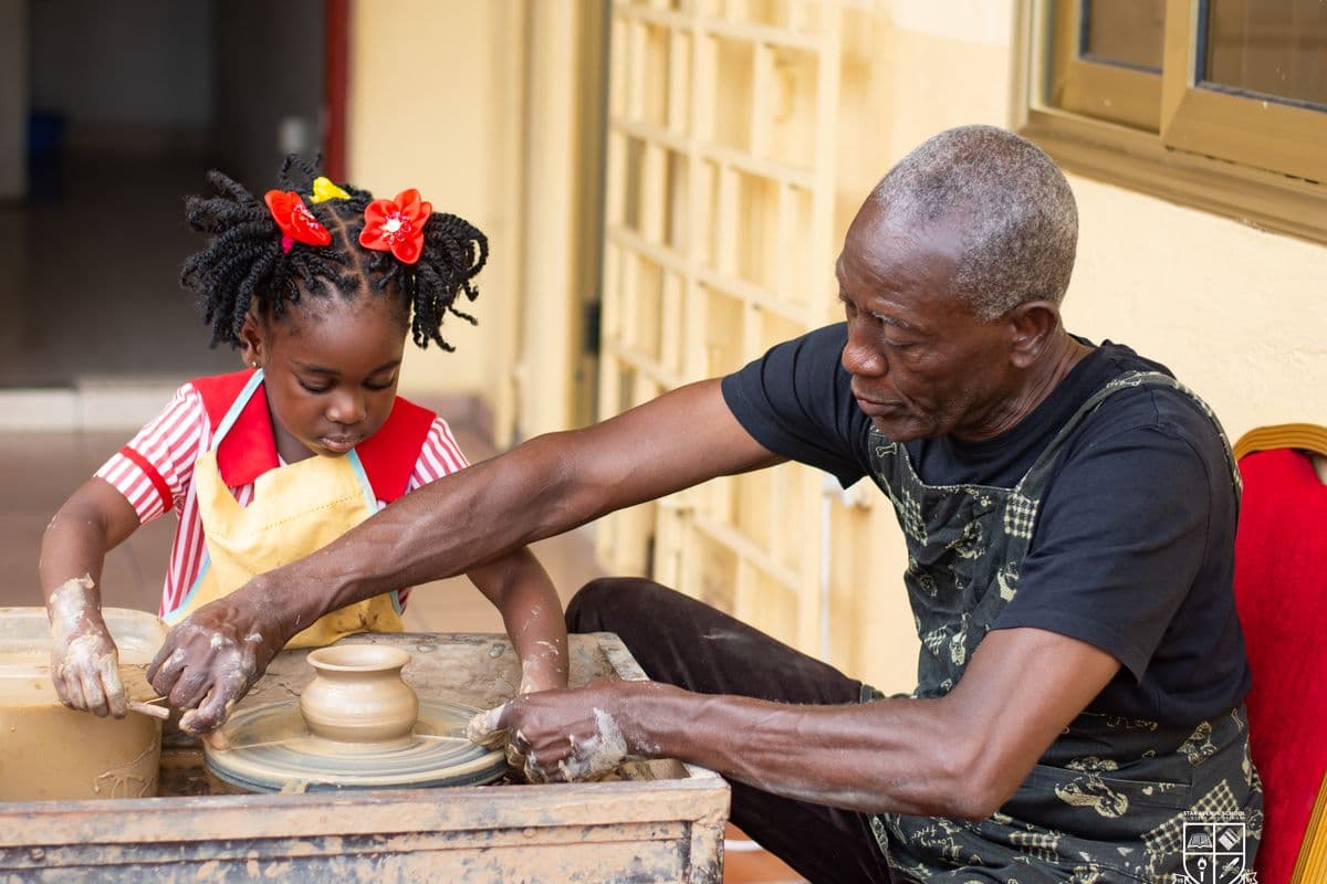 A visiting potter guiding a pupil at the wheel
