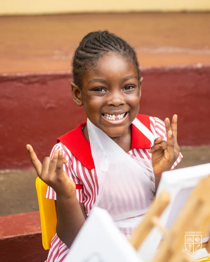 A preschooler in a painting apron, hands raised, grinning at the camera