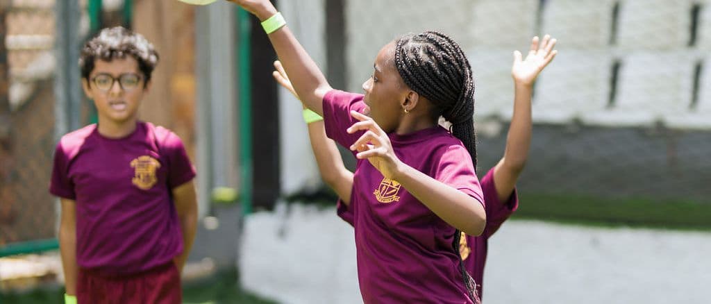 A pupil in school uniform reaching up to catch a ball during games