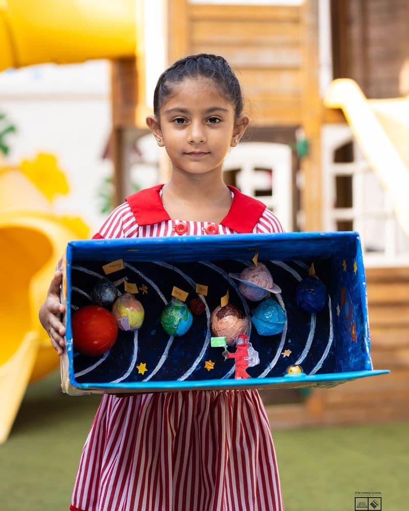 A pupil holding a hand-built model of the solar system
