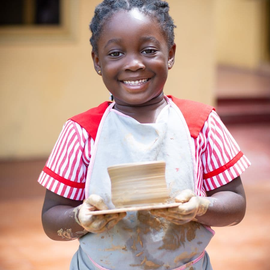 A pupil beaming as she holds the clay bowl she has just made