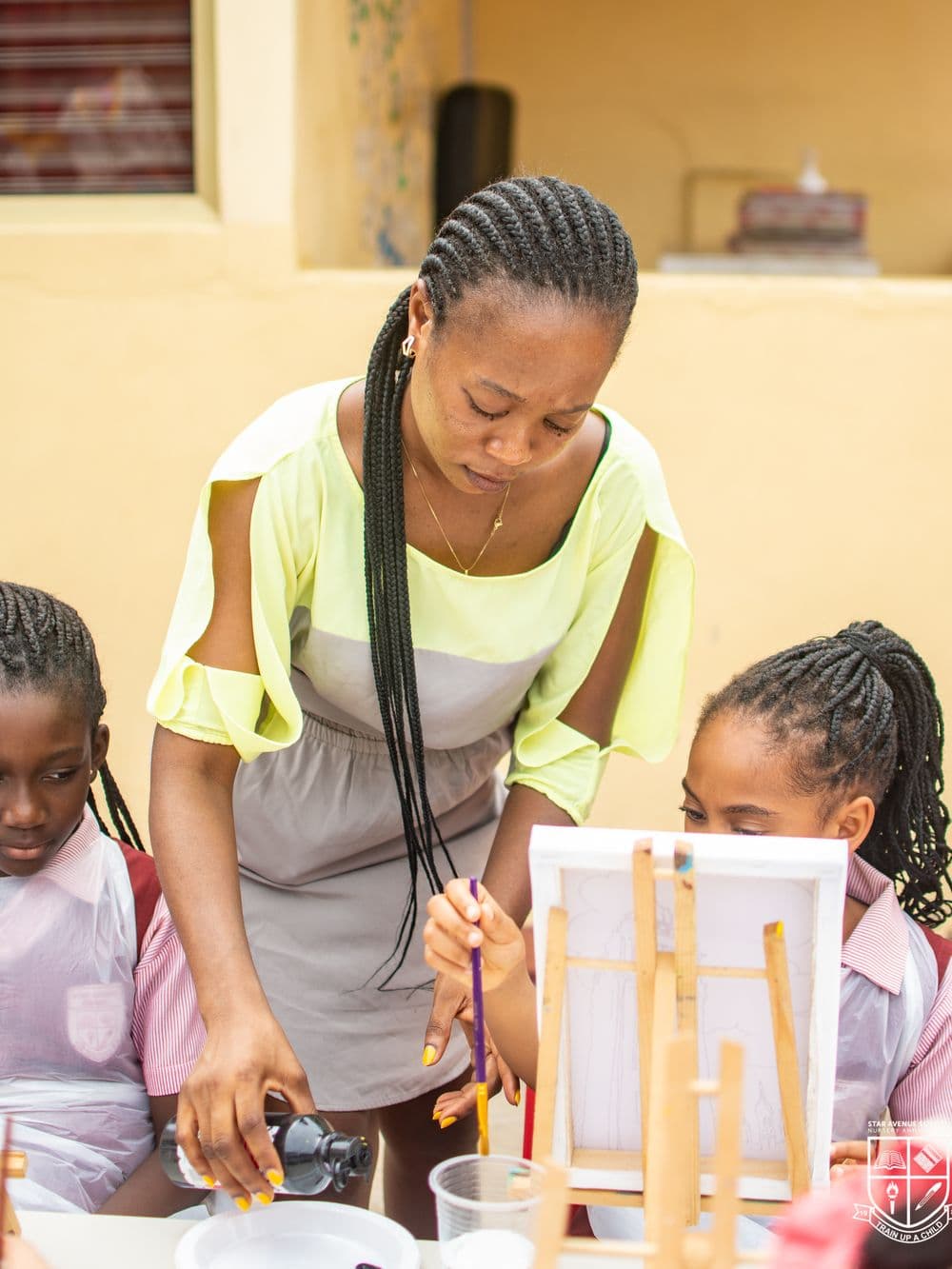 A teacher leaning in between two pupils at their easels during a painting session