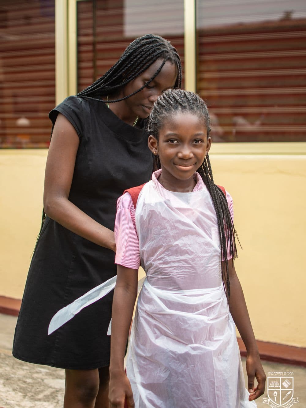 A member of staff tying a painting apron for a pupil in the courtyard