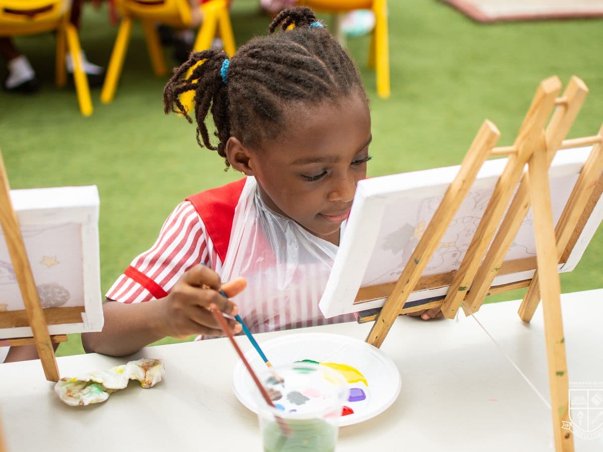 A young pupil painting at an easel on the school lawn