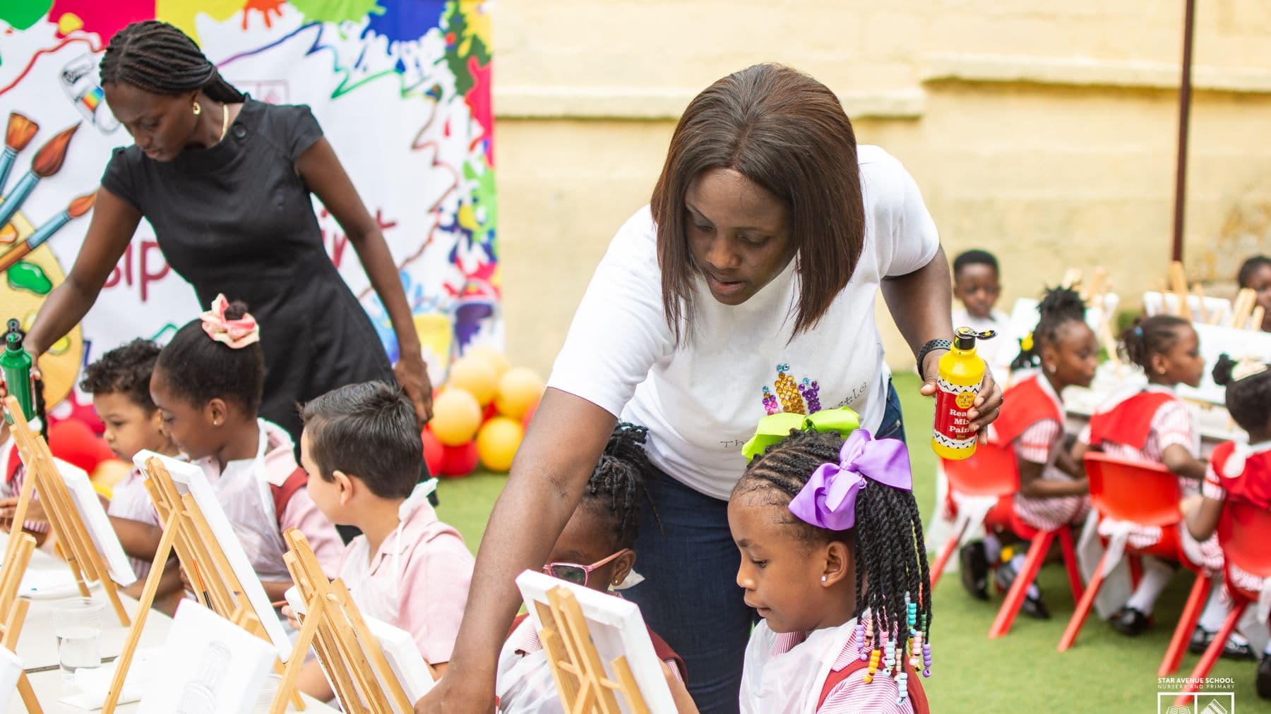 A teacher moving between easels to help pupils with their paintings